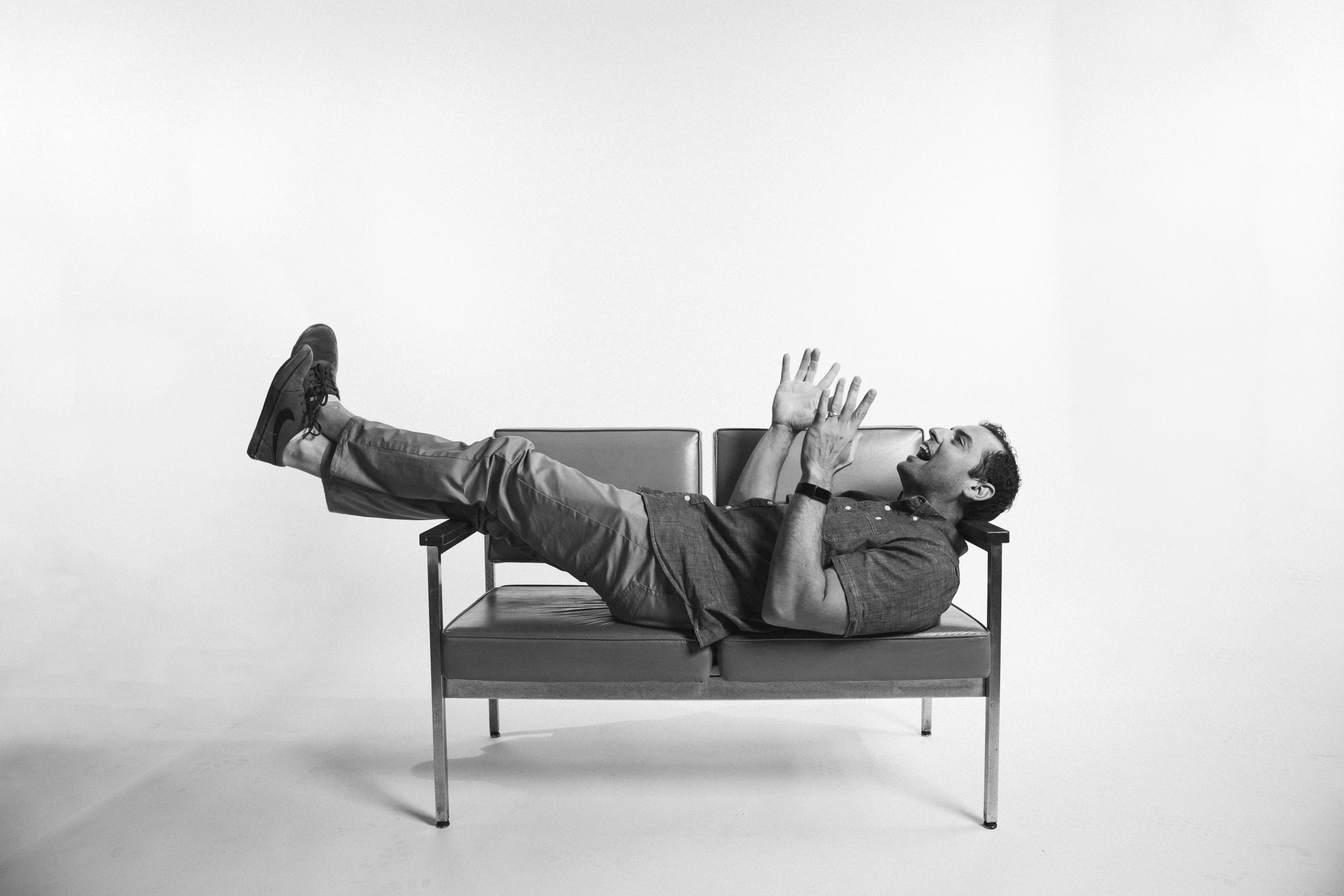 Morgan Myer laying on a couch with hands in the air - B&W